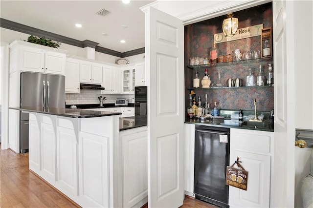 kitchen featuring under cabinet range hood, white cabinetry, visible vents, freestanding refrigerator, and dark countertops