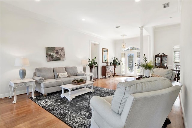 living area with ornate columns, light wood-style flooring, visible vents, and crown molding