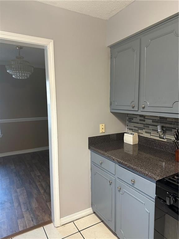 kitchen featuring a chandelier, black electric range oven, light hardwood / wood-style flooring, backsplash, and gray cabinetry