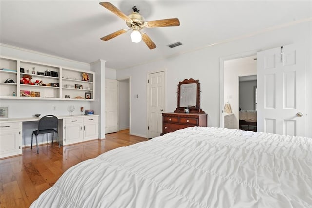 bedroom featuring light hardwood / wood-style flooring, built in desk, ceiling fan, and connected bathroom