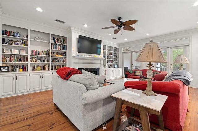 living room with light hardwood / wood-style flooring, ceiling fan, crown molding, and built in features