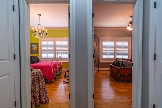 bedroom featuring multiple windows, crown molding, light hardwood / wood-style floors, and an inviting chandelier