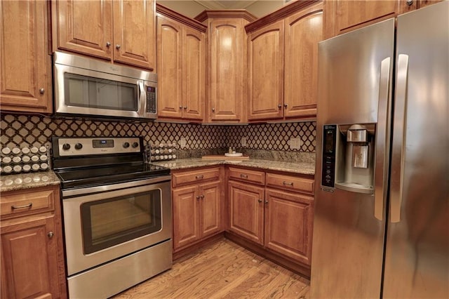 kitchen featuring light stone counters, appliances with stainless steel finishes, light hardwood / wood-style floors, and tasteful backsplash