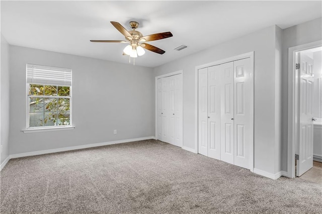 unfurnished bedroom featuring multiple closets, ceiling fan, ensuite bath, and light colored carpet