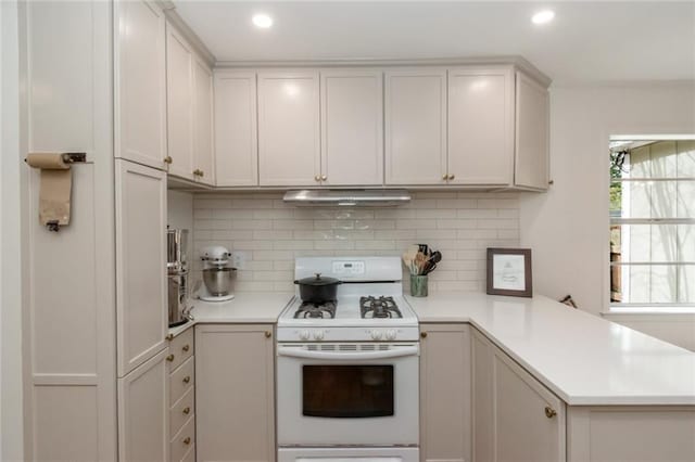 kitchen with white range with gas cooktop, a peninsula, decorative backsplash, light countertops, and under cabinet range hood