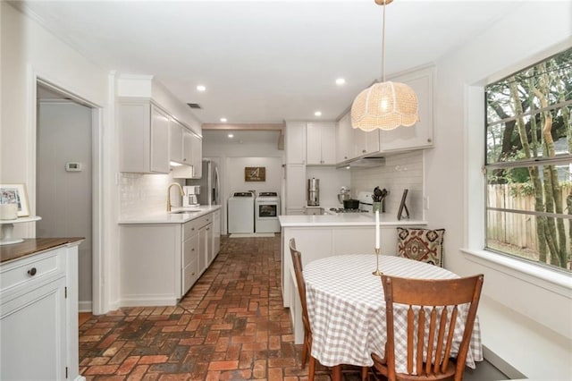 kitchen with separate washer and dryer, brick floor, a sink, decorative backsplash, and white cabinetry