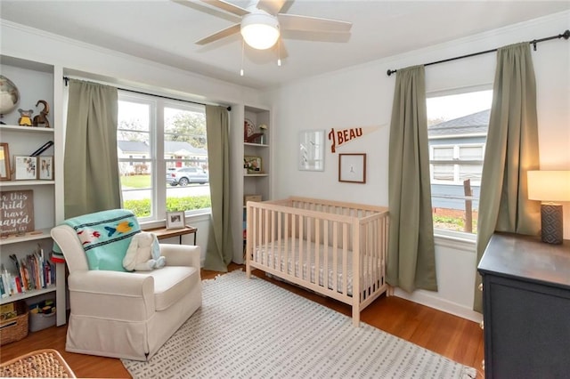 bedroom featuring multiple windows, a crib, ceiling fan, and wood finished floors