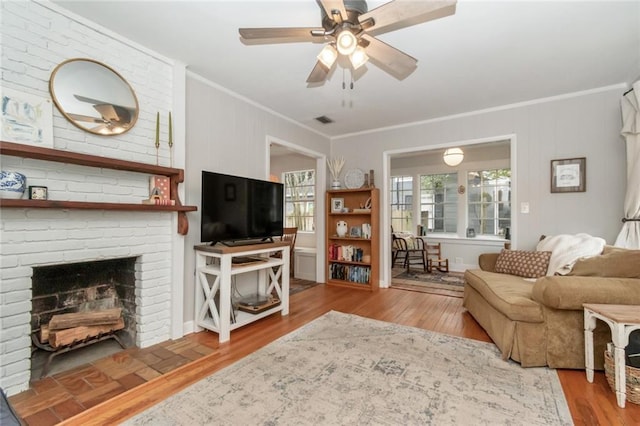 living area featuring visible vents, ornamental molding, wood finished floors, a fireplace, and ceiling fan