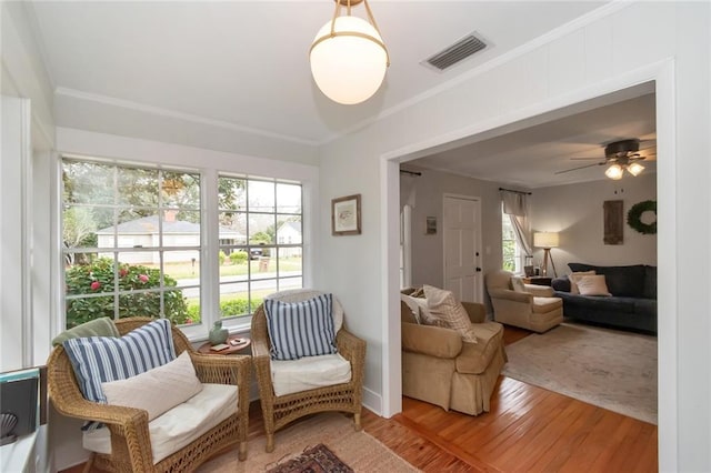 sitting room with visible vents, wood finished floors, a ceiling fan, and ornamental molding