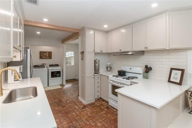 kitchen with under cabinet range hood, white range with gas cooktop, decorative backsplash, washer and dryer, and a sink