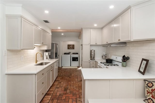 kitchen with under cabinet range hood, washing machine and dryer, range, brick floor, and a sink