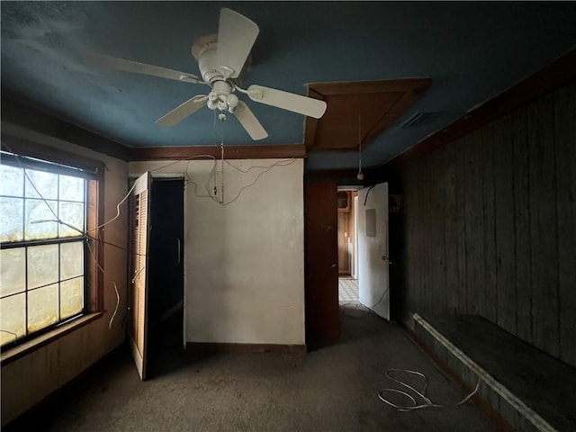 unfurnished bedroom with carpet floors, wooden walls, and ceiling fan