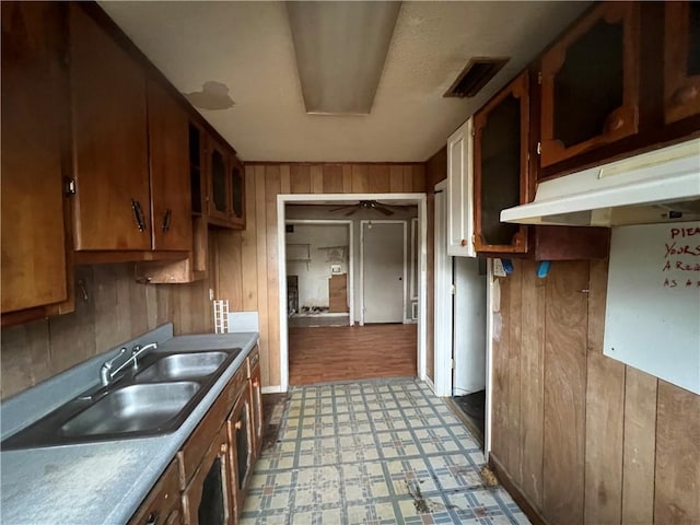 kitchen with ceiling fan, wooden walls, sink, and light hardwood / wood-style flooring