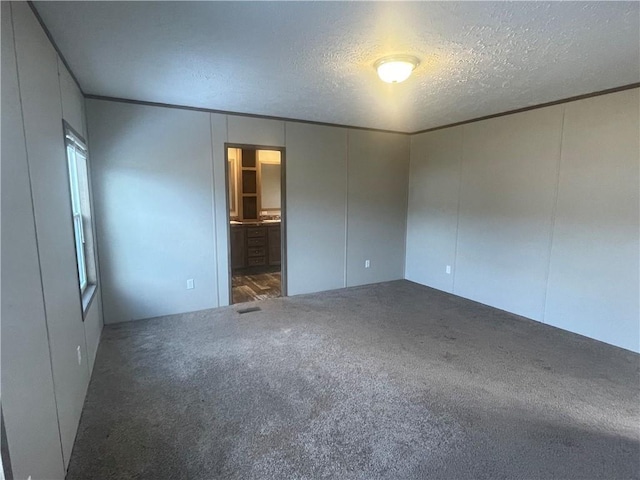 unfurnished bedroom featuring connected bathroom, a textured ceiling, and dark carpet