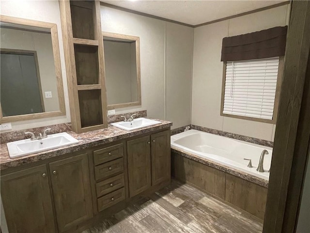 bathroom featuring hardwood / wood-style flooring, vanity, a relaxing tiled tub, ornamental molding, and a textured ceiling