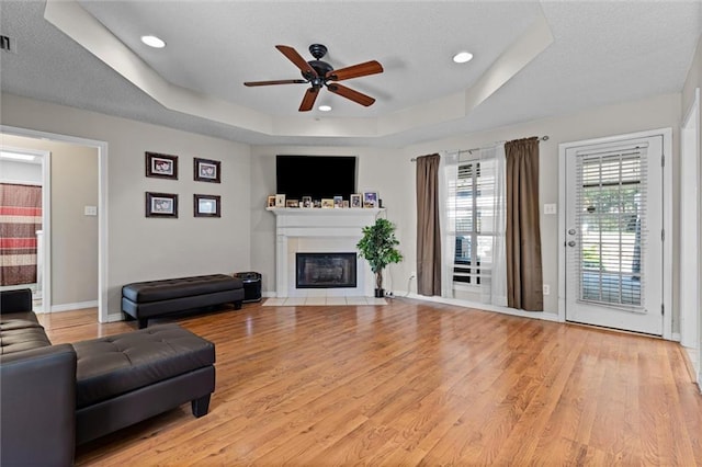 living room featuring ceiling fan, light hardwood / wood-style floors, and a tray ceiling