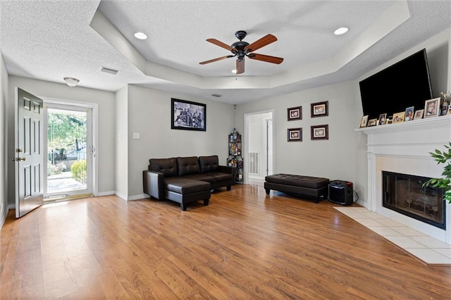 living room featuring a textured ceiling, ceiling fan, light hardwood / wood-style flooring, and a tray ceiling