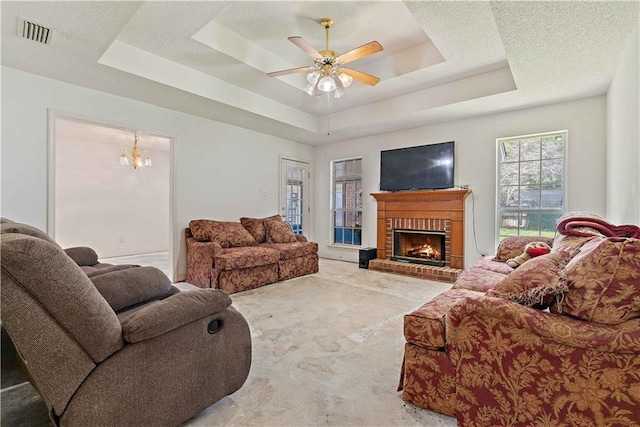 living room with a tray ceiling, a textured ceiling, a fireplace, and ceiling fan with notable chandelier