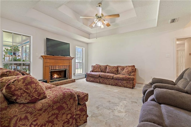 carpeted living room featuring a textured ceiling, ceiling fan, a raised ceiling, and a fireplace