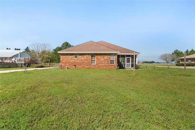 exterior space featuring a sunroom, fence, brick siding, and a yard