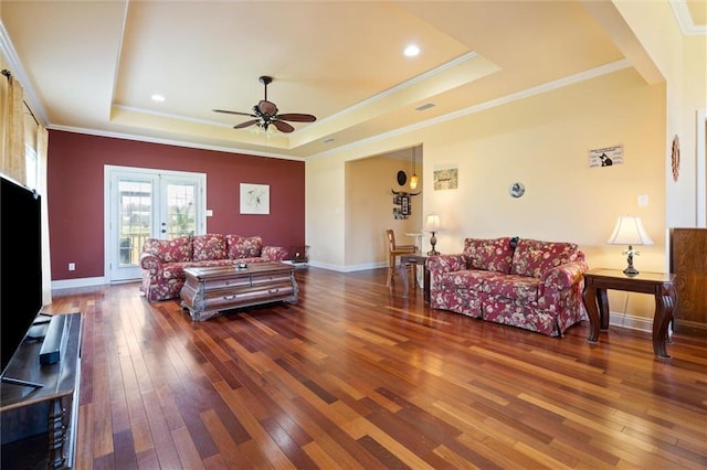 living room featuring crown molding, hardwood / wood-style flooring, baseboards, a ceiling fan, and a raised ceiling