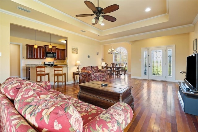 living room with a tray ceiling, visible vents, ornamental molding, and dark wood finished floors