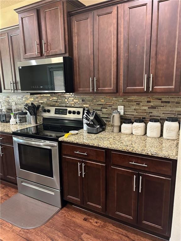 kitchen with dark brown cabinetry, dark wood finished floors, light stone counters, appliances with stainless steel finishes, and backsplash