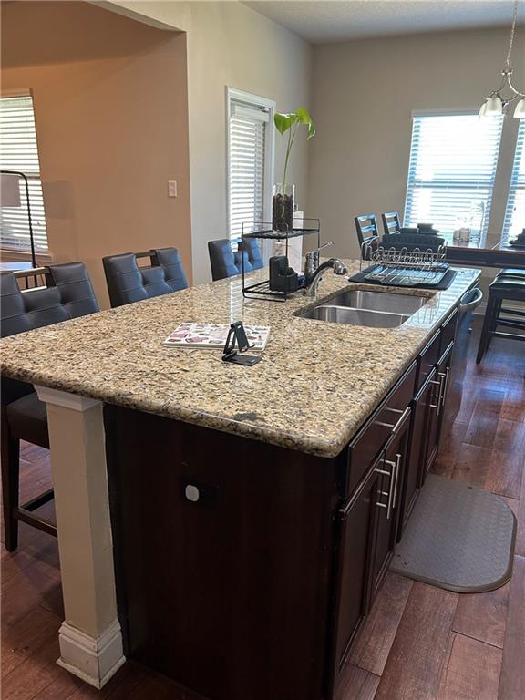 kitchen with dark wood-style floors, a breakfast bar area, a sink, and a kitchen island with sink