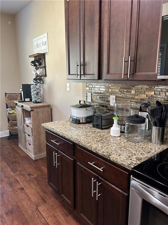 kitchen featuring electric stove, dark wood-style flooring, decorative backsplash, dark brown cabinets, and light stone countertops