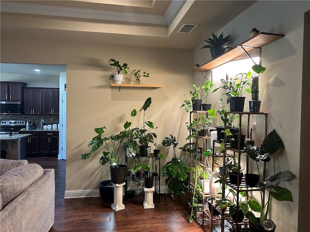 interior space featuring baseboards, visible vents, a raised ceiling, dark wood-style floors, and ornamental molding