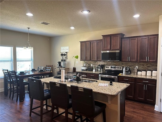 kitchen with appliances with stainless steel finishes, visible vents, dark wood finished floors, and tasteful backsplash