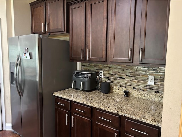 kitchen featuring tasteful backsplash, dark brown cabinets, light stone counters, and stainless steel fridge with ice dispenser