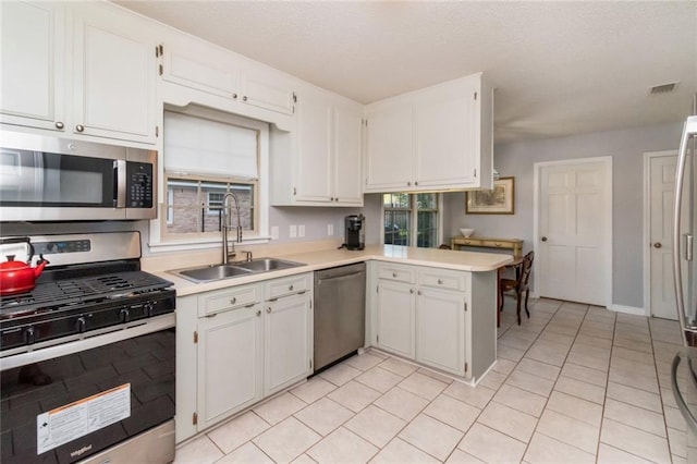 kitchen featuring a peninsula, white cabinetry, appliances with stainless steel finishes, light countertops, and a sink