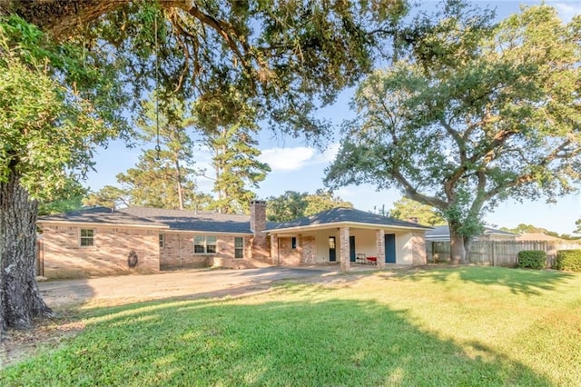 back of property featuring a carport, a chimney, fence, and a lawn