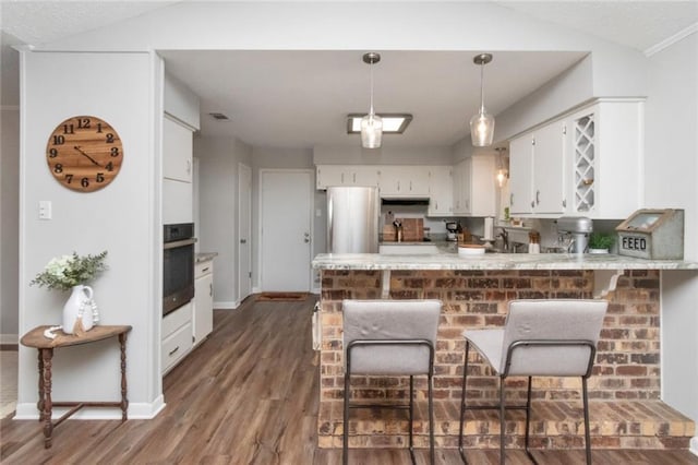 kitchen with kitchen peninsula, appliances with stainless steel finishes, vaulted ceiling, white cabinets, and dark hardwood / wood-style floors