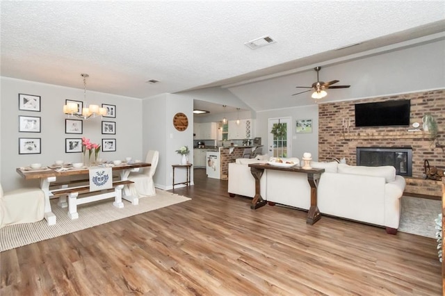 living room featuring hardwood / wood-style flooring, ceiling fan with notable chandelier, a fireplace, and vaulted ceiling