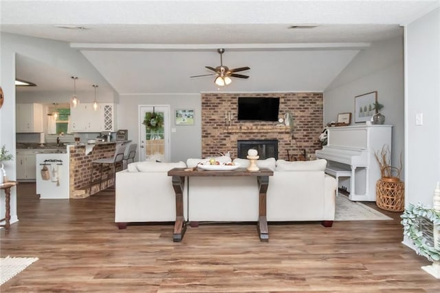 living room with ceiling fan, a fireplace, lofted ceiling with beams, and wood-type flooring