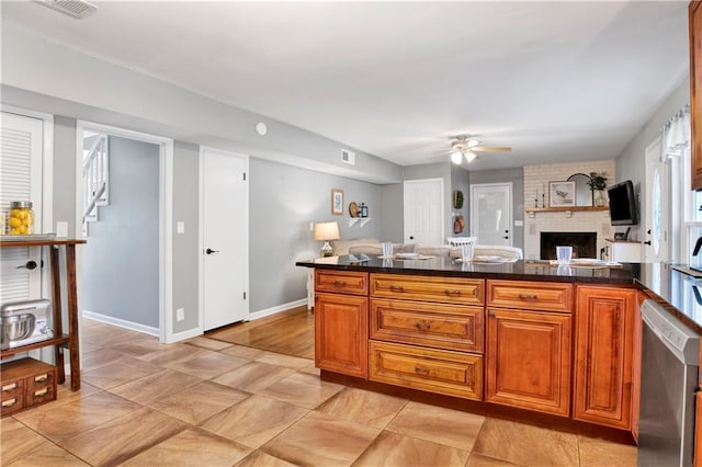 kitchen with stainless steel dishwasher, ceiling fan, visible vents, a fireplace, and brown cabinetry