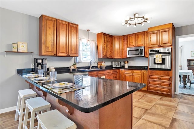 kitchen with brown cabinetry, stainless steel appliances, a kitchen bar, a sink, and a peninsula