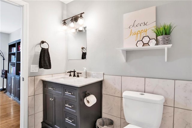 bathroom featuring tile walls, vanity, toilet, wainscoting, and wood finished floors
