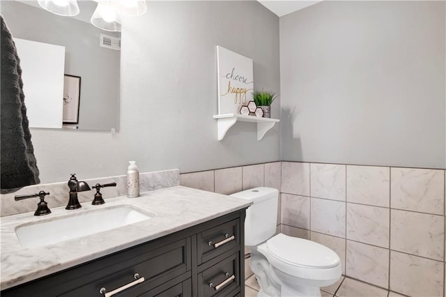half bathroom with wainscoting, tile walls, toilet, vanity, and visible vents