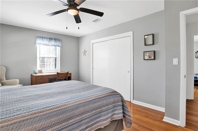 bedroom with visible vents, a closet, baseboards, wood finished floors, and a ceiling fan