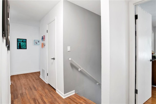 hall with an upstairs landing, visible vents, wood finished floors, and baseboards