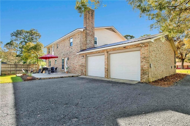 view of property exterior featuring driveway, a chimney, an attached garage, fence, and brick siding