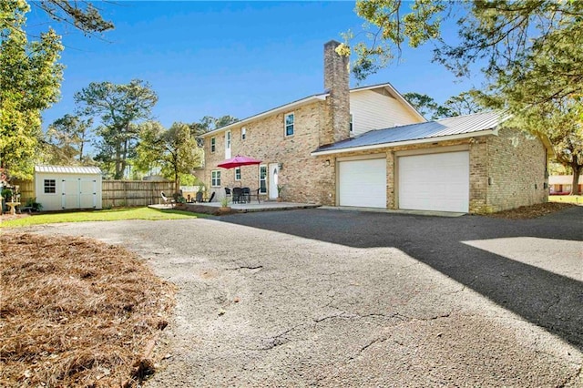 rear view of property with a chimney, an outdoor structure, a storage unit, brick siding, and an attached garage