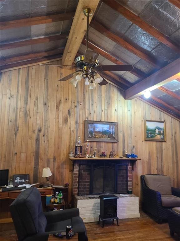 living area with lofted ceiling with beams, a wood stove, a ceiling fan, wooden walls, and wood finished floors