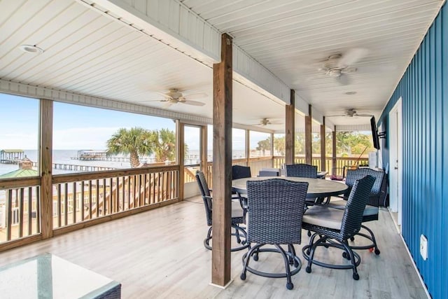 wooden terrace with a ceiling fan, outdoor dining space, and a water view