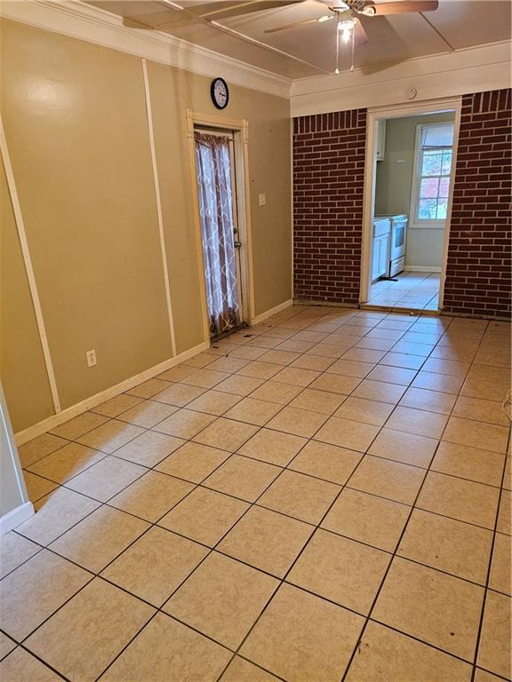 spare room with ceiling fan, light tile patterned flooring, crown molding, and brick wall