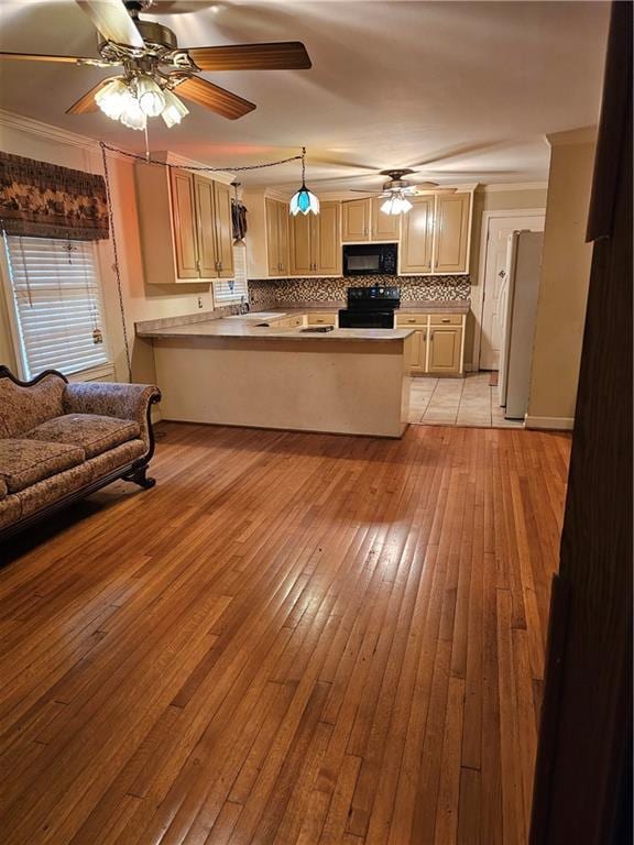 kitchen featuring kitchen peninsula, crown molding, light hardwood / wood-style floors, decorative backsplash, and black appliances