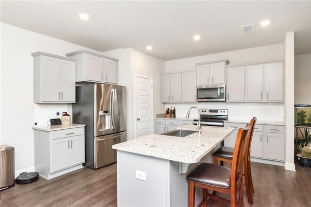 kitchen with dark wood-type flooring, a center island with sink, sink, light stone countertops, and stainless steel appliances